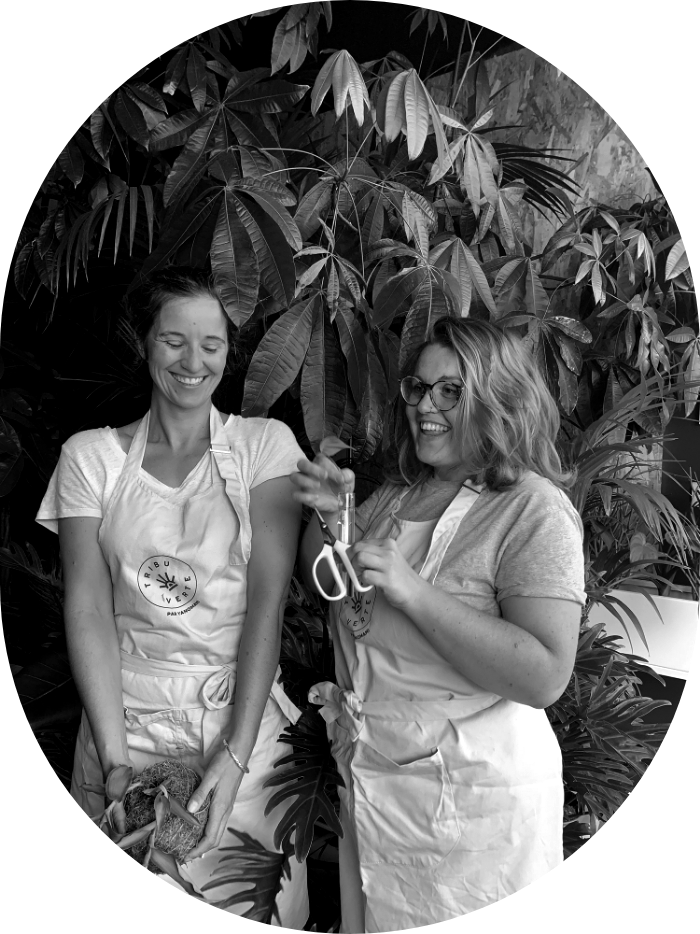 Photo noir et blanc de deux femmes rigolant, portant des tabliers, avec en fond une grande plante.